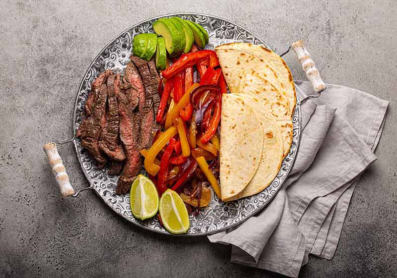 where to stay in roma mexico city Traditional Mexican dish Beef fajita served with tortillas and ripe avocado on rustic metal plate and stone background from above